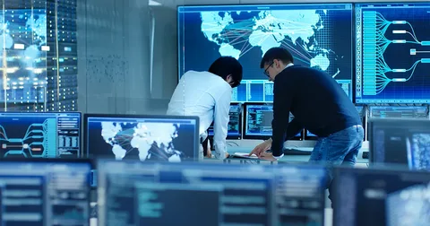 Security consulting services team collaborating at a network operations desk, studying world maps and data screens in a high-tech control room.